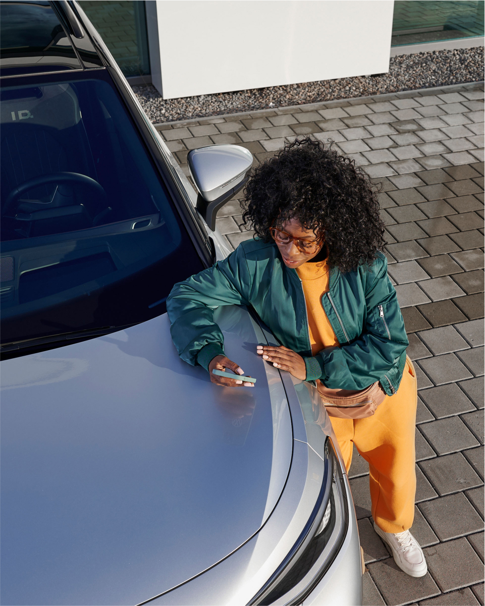 Persona apoyada en un vehículo Volkswagen que sostiene un teléfono celular